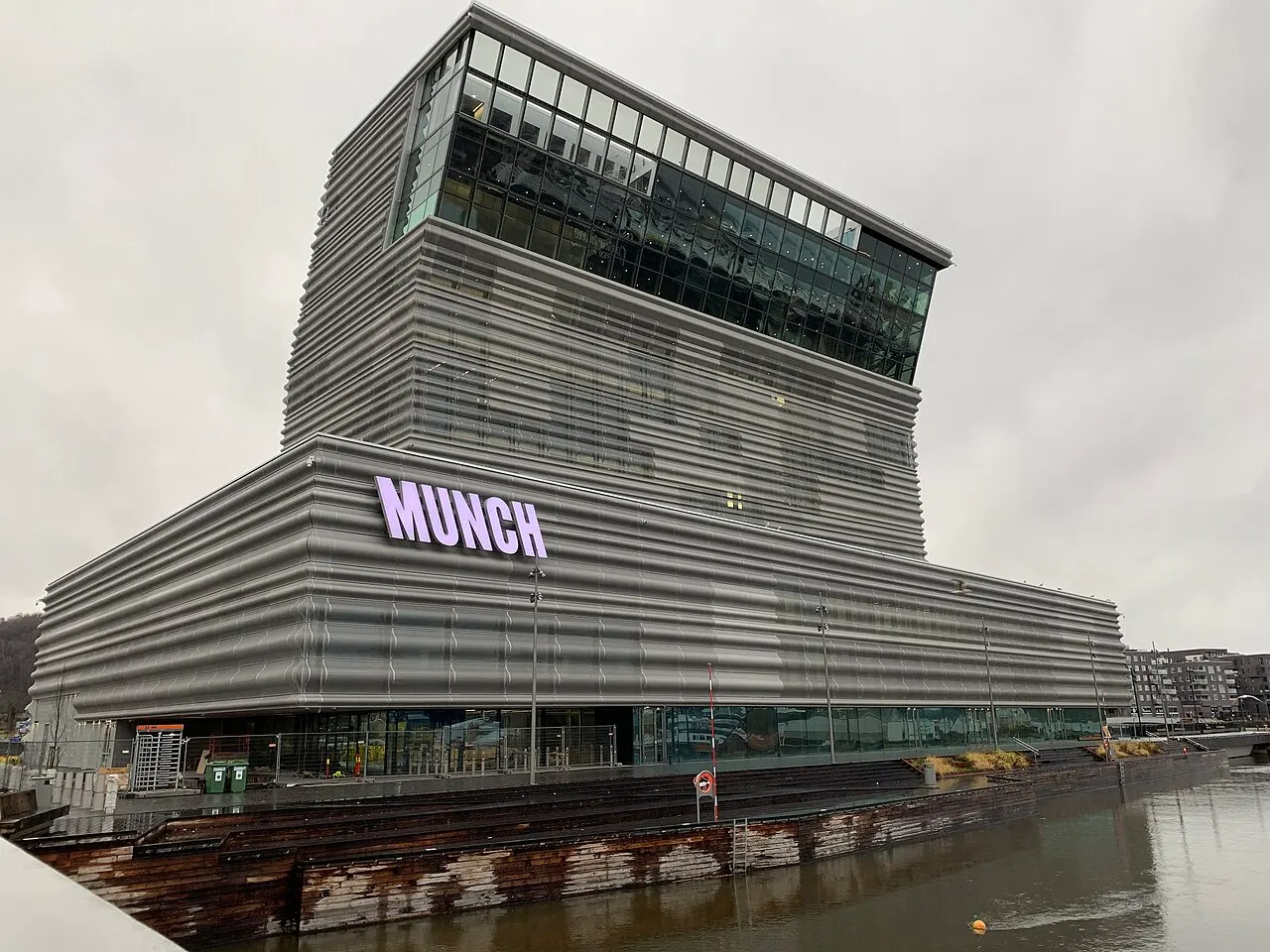 Museu MUNCH, em Oslo, torre cinza de fachada perfurada com o topo inclinado sobre a entrada.