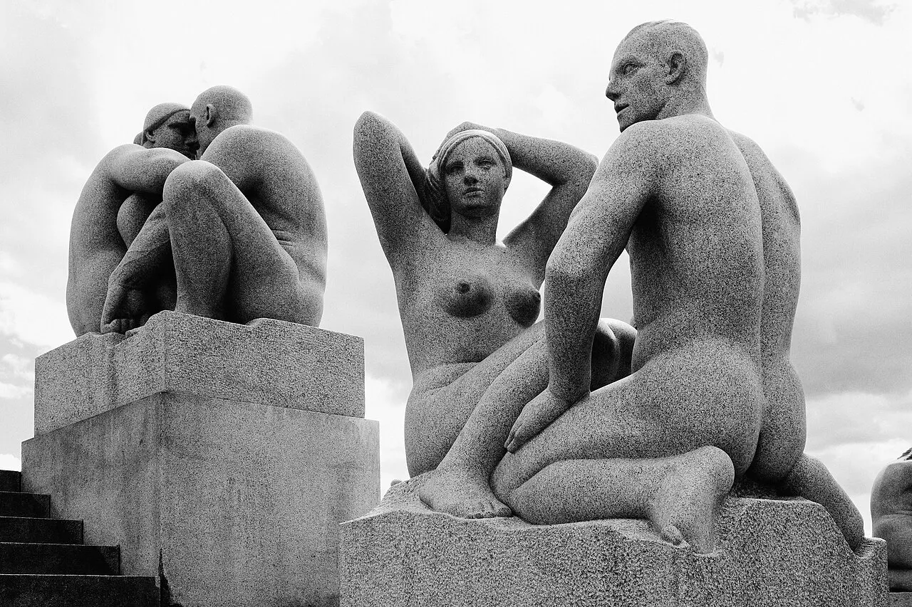 Photographie en noir et blanc de sculptures en granit représentant des figures humaines nues assises sur des socles au Vigelandsparken, sous un ciel nuageux.
