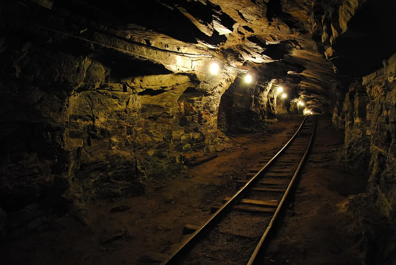 A galeria da Mina da Passagem, um túnel escavado na rocha com trilhos no chão e lâmpadas ao longo do teto.