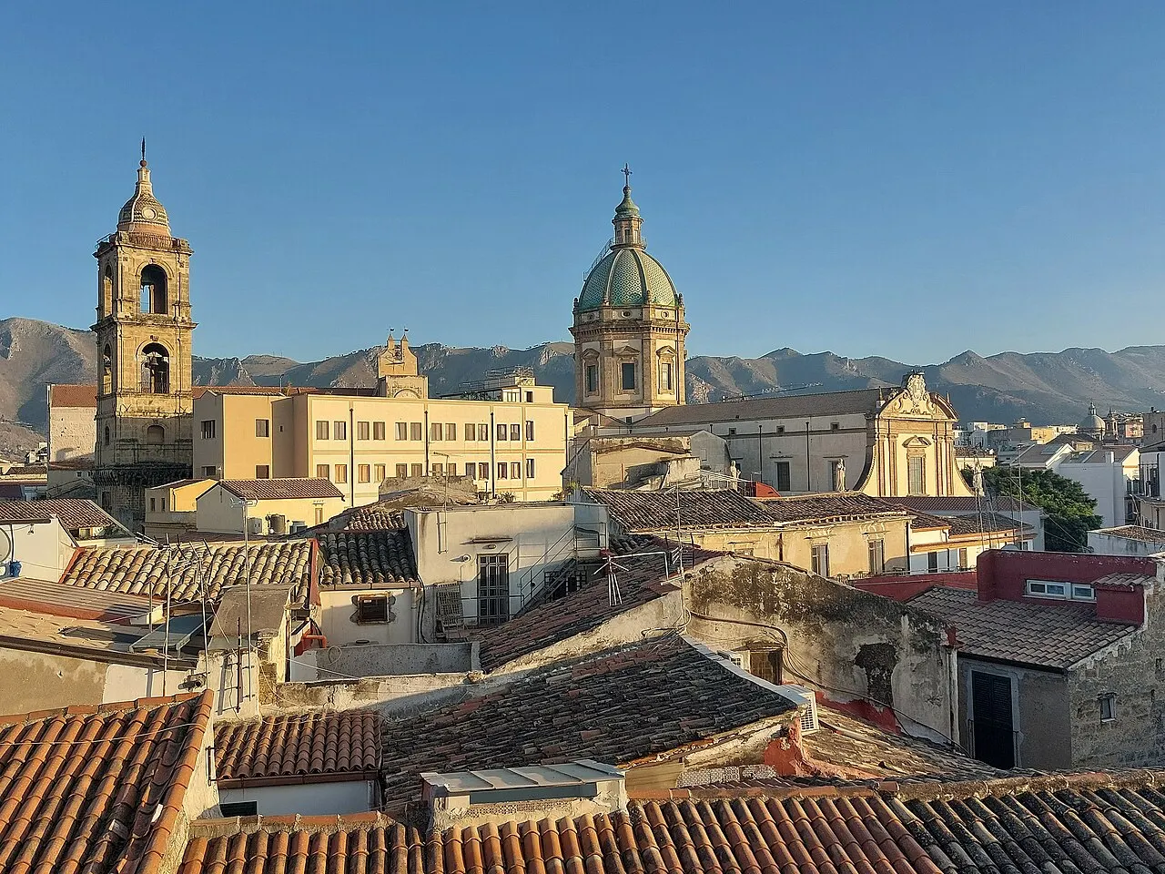 Os telhados de Palermo vistos do alto, com a cúpula verde e o campanário da Igreja do Gesù e montanhas atrás.