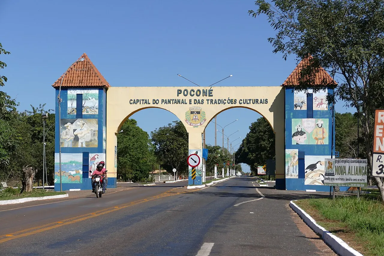 O portal de entrada de Poconé sobre a estrada, com duas torres pintadas e o letreiro da cidade no arco.