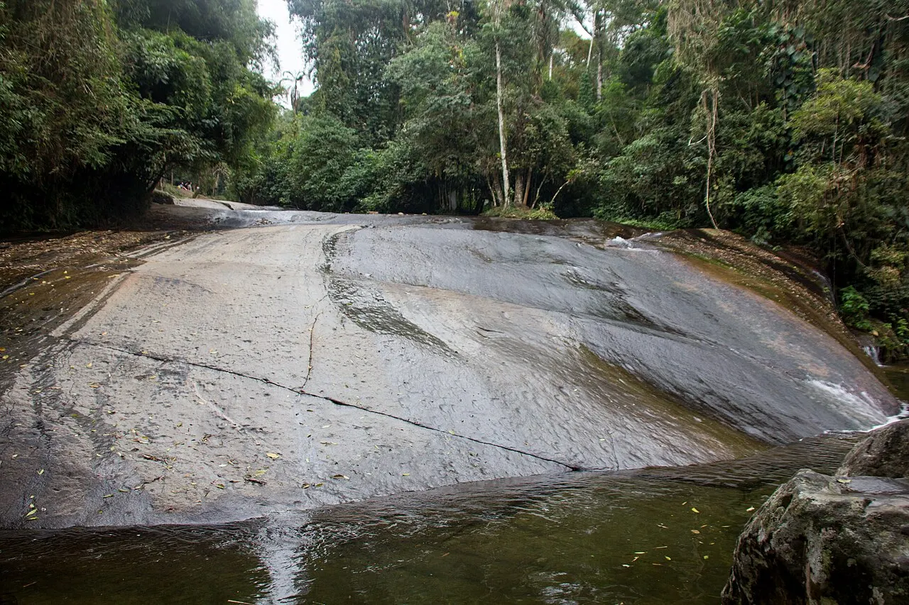 A Cachoeira do Tobogã, uma laje de pedra lisa e inclinada por onde a água escorre até um poço, cercada pela mata.