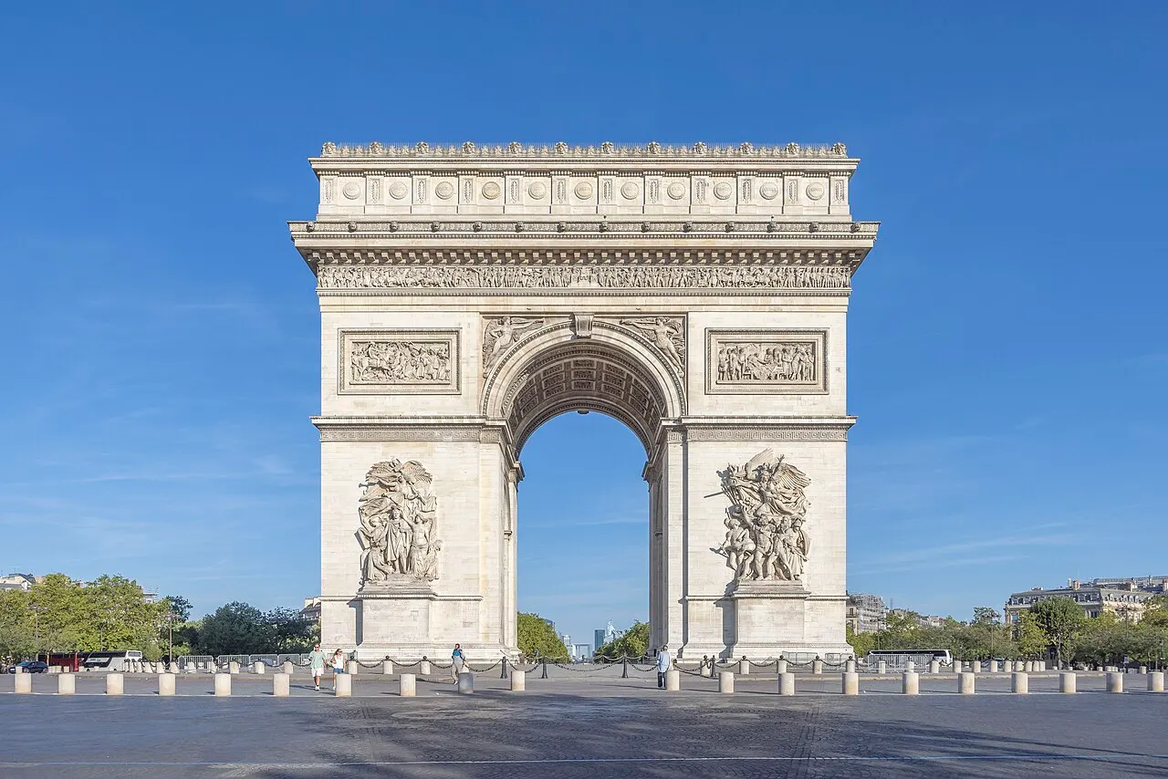 Arco monumental de pedra clara com grandes relevos nos pilares, contra o céu azul.