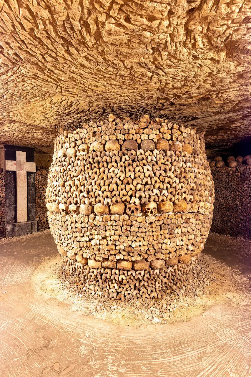 Coluna em forma de barril feita de crânios e ossos empilhados, numa galeria de calcário.