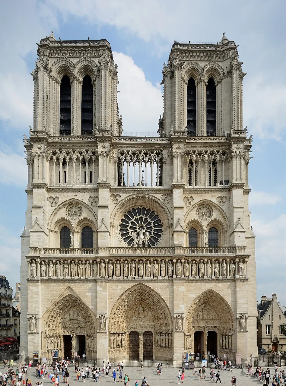 Fachada gótica de Notre-Dame com duas torres quadradas, a rosácea e três portais, com gente no adro.