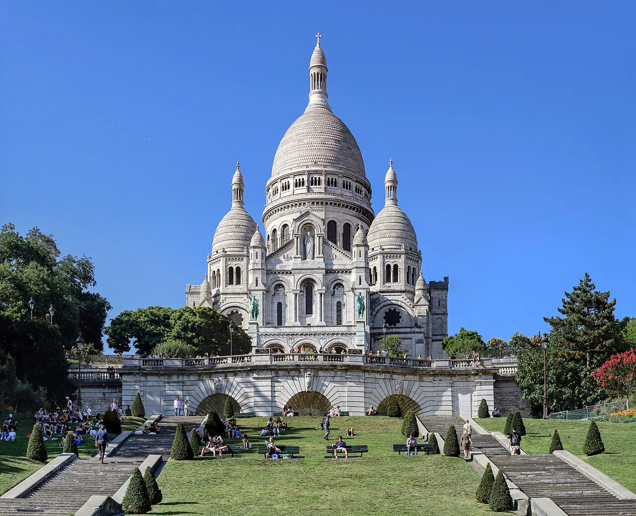 Basílica branca com domo central e cúpulas menores no alto de Montmartre, sobre um terraço de pedra.
