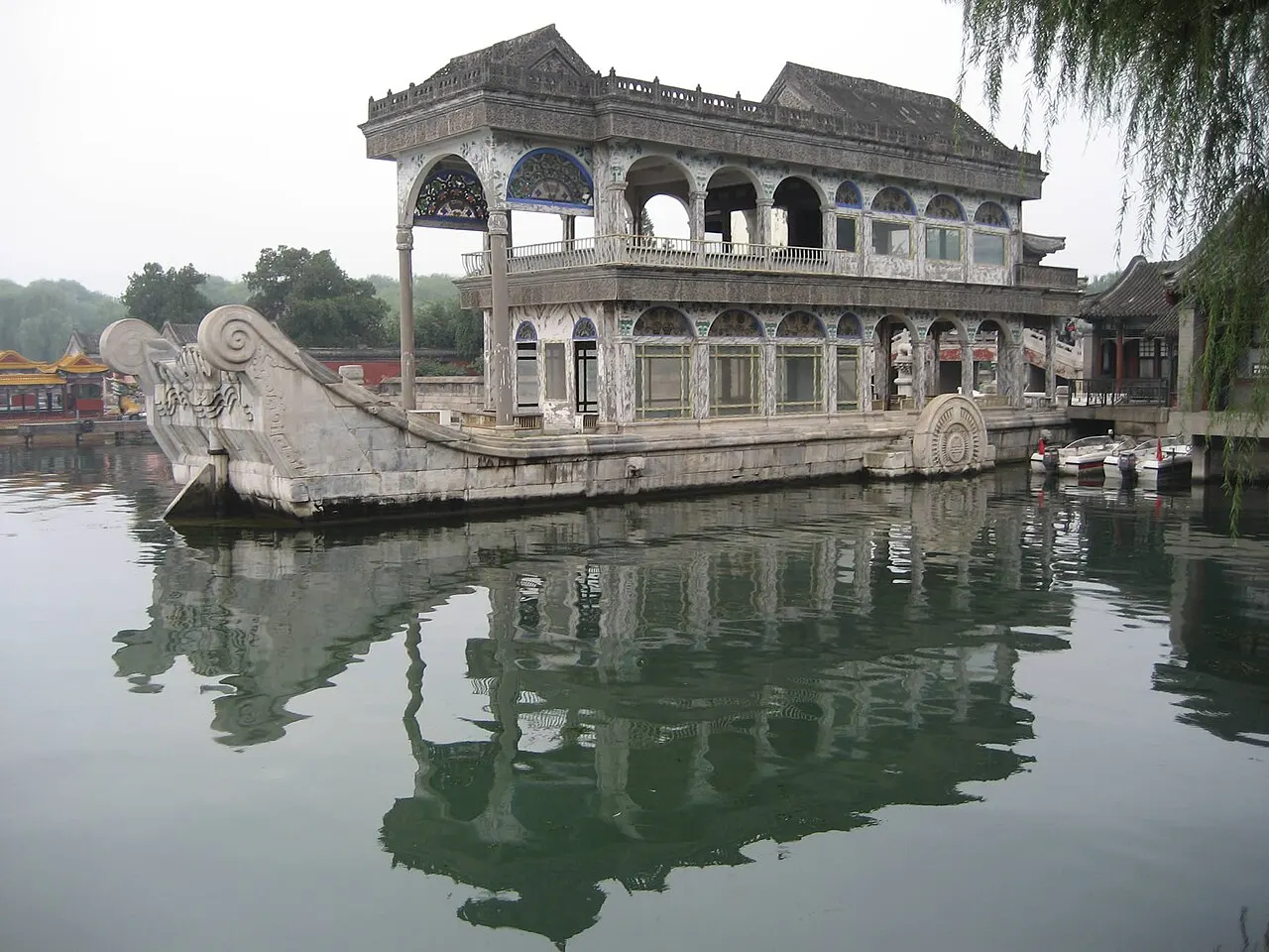 Pavilhão de dois andares com arcos e janelas sobre um casco de pedra em forma de barco, na beira do lago.