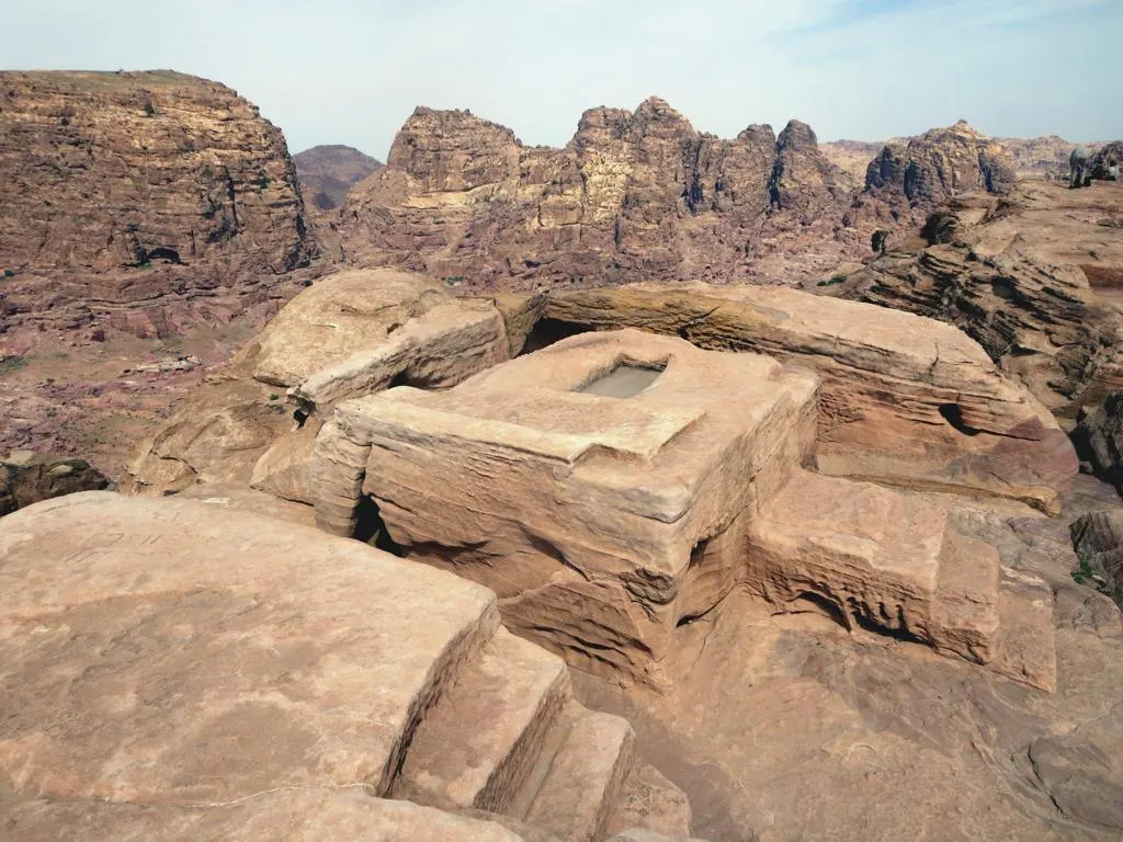 Altar e bacias talhados na rocha nua do Alto Lugar do Sacrifício, no topo de Petra, com os paredões e os vales de arenito estendendo-se ao fundo.