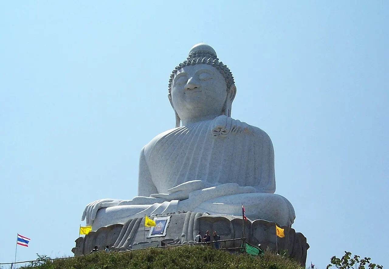 O Grande Buda de Phuket, estátua sentada de mármore branco no alto do morro, contra o céu azul.