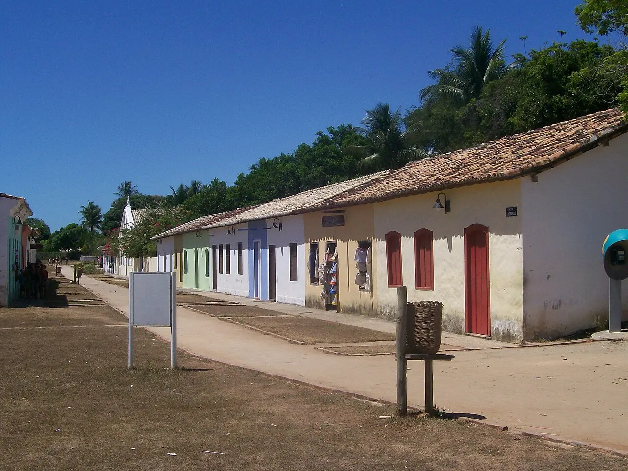 Uma fileira de casas coloniais térreas, de portas coloridas, na Cidade Histórica de Porto Seguro, com o gramado e o céu azul à frente.