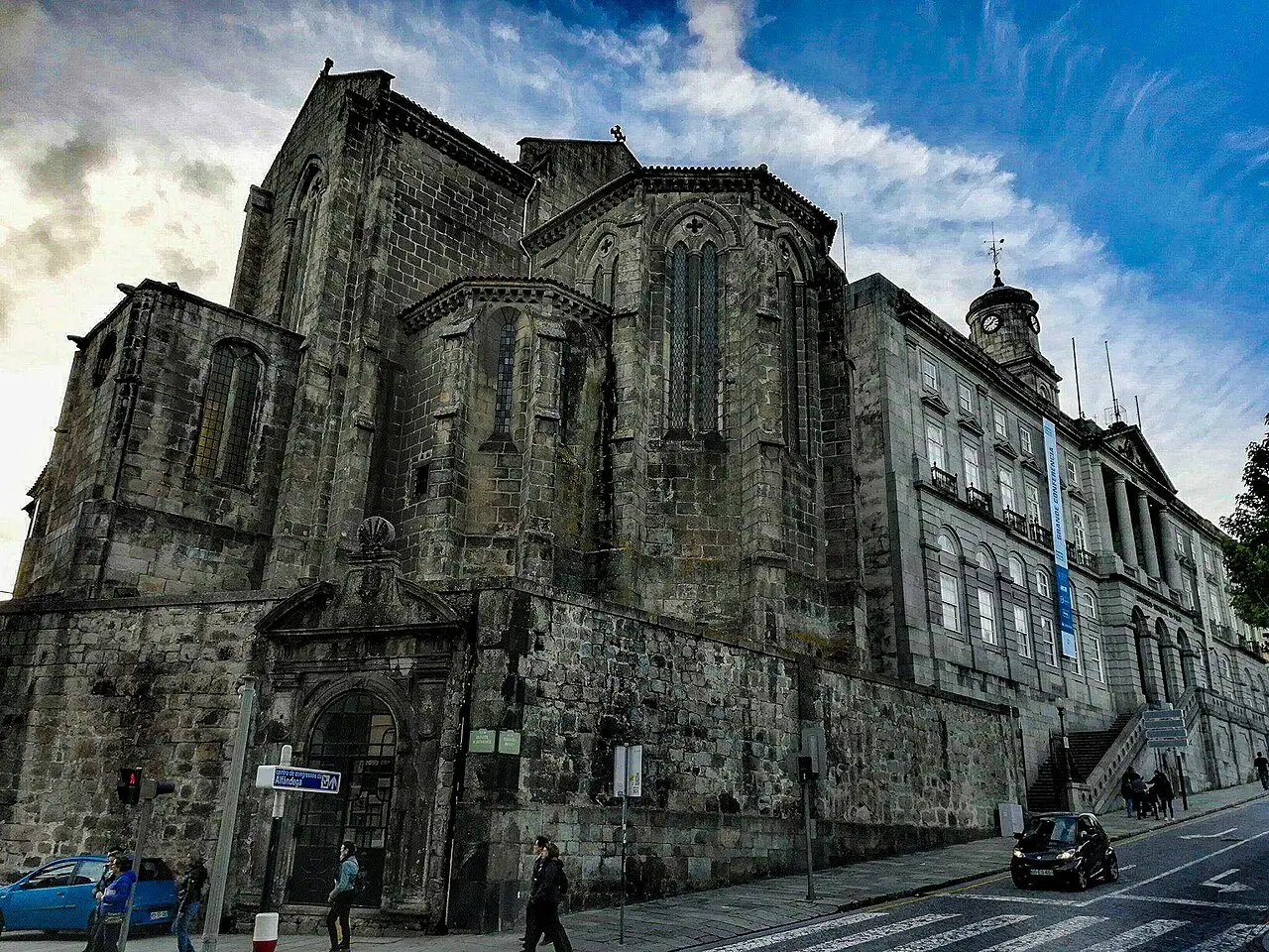 Lateral gótica de pedra escura da Igreja de São Francisco, vista da rua sob um céu com nuvens.