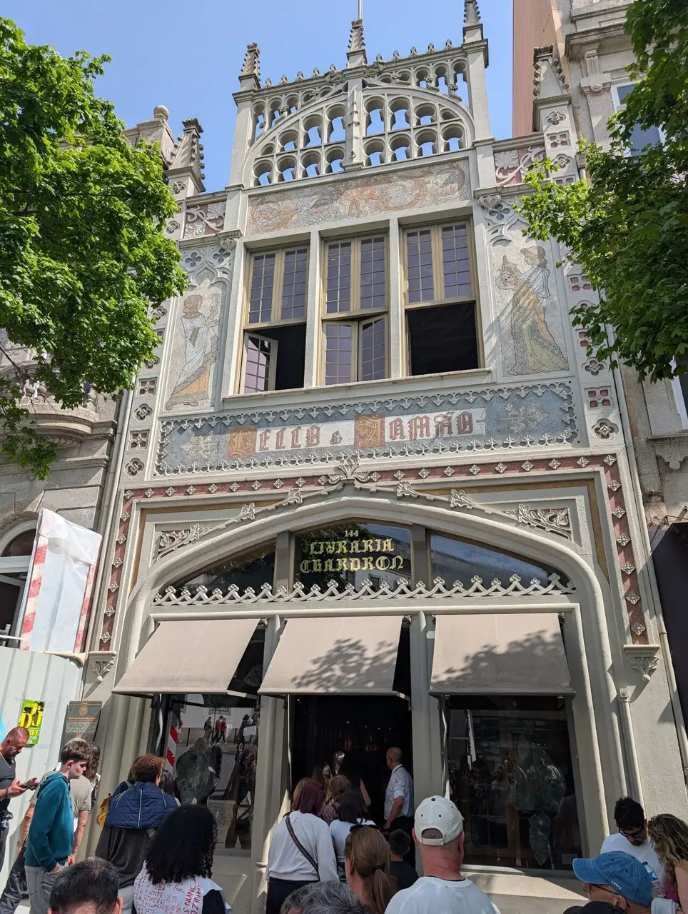 Fachada da Livraria Lello, estreita e neogótica, com o nome sobre o arco da entrada e gente na calçada.