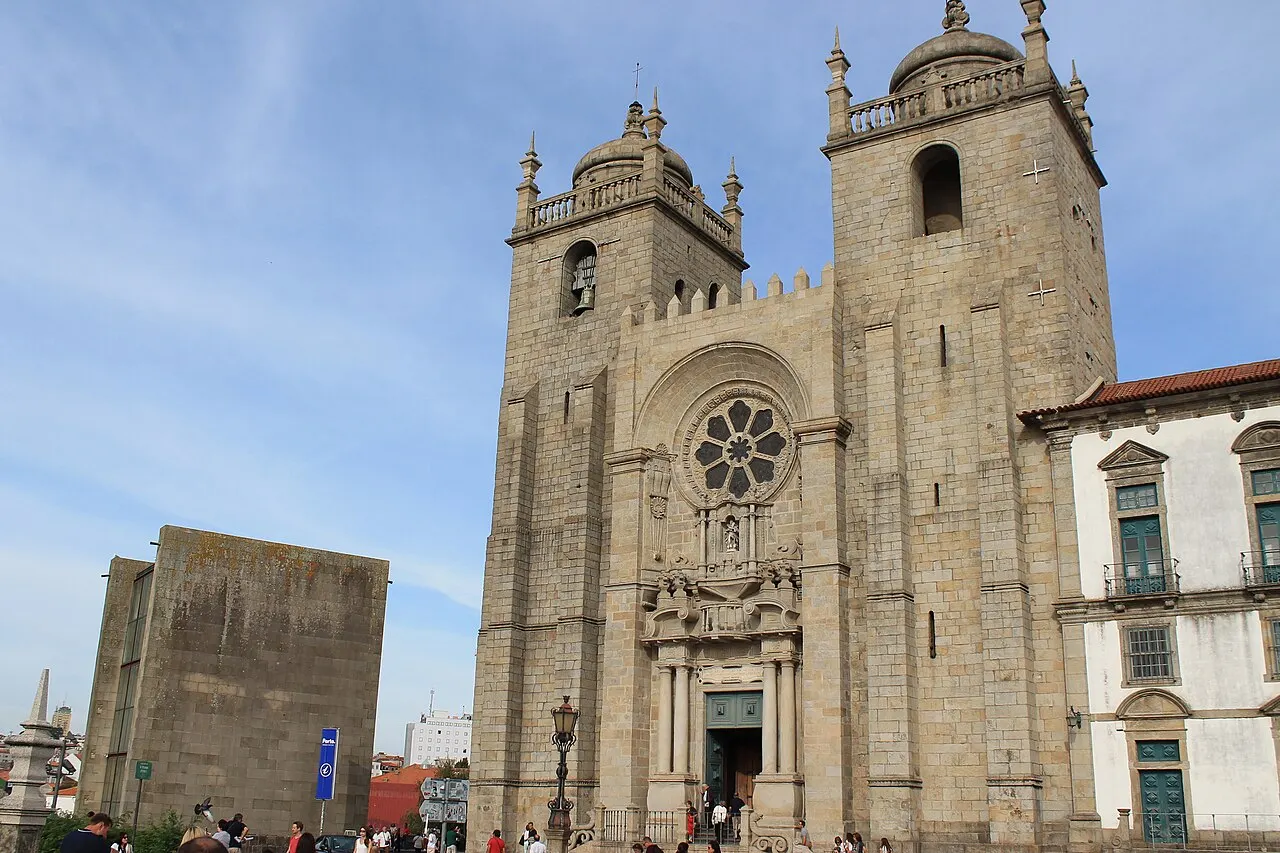 Fachada de granito da Sé do Porto, com duas torres e uma rosácea, vista do largo sob céu azul.