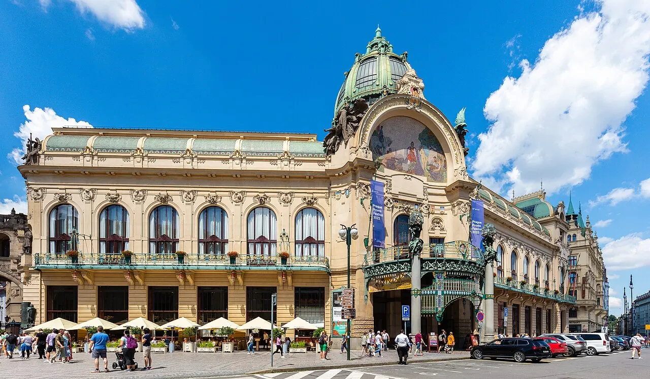 Fachada art nouveau da Casa Municipal, com cúpula verde e mesas de café na praça, sob céu azul.