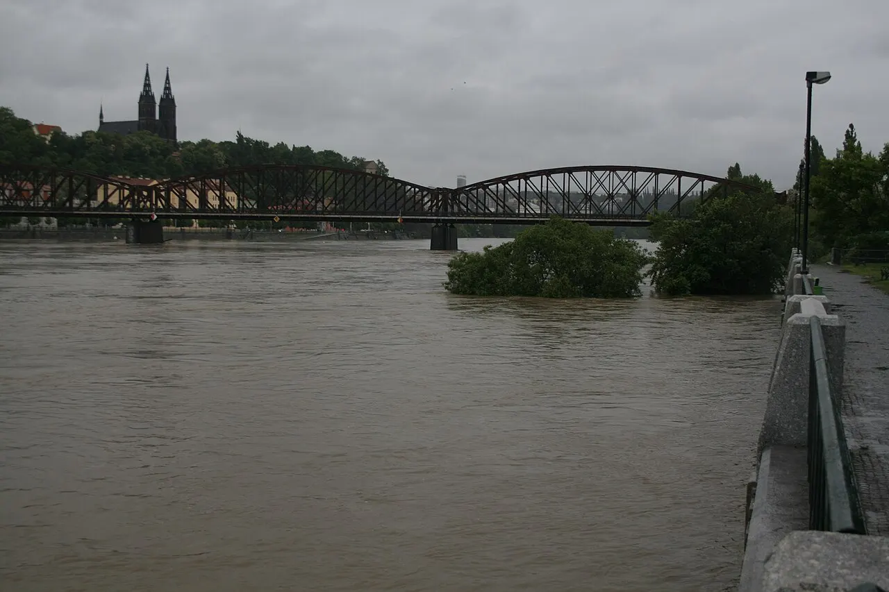 Vyšehrad hill with the basilica on top, above the swollen Vltava River, with an iron bridge to the left.