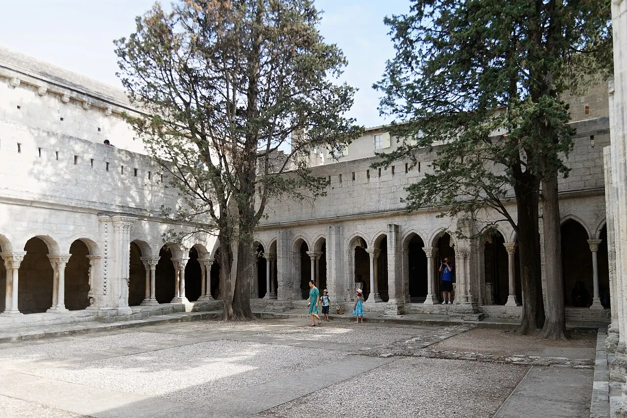 O pátio do claustro de Saint-Trophime, com as arcadas românicas de colunas duplas e duas árvores altas no meio.