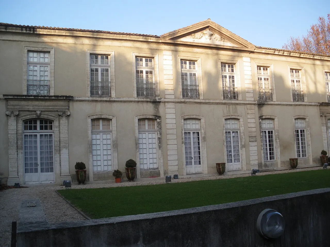 A fachada clássica e clara do Hôtel de Caumont, com janelas altas, vasos na frente e o gramado do pátio.