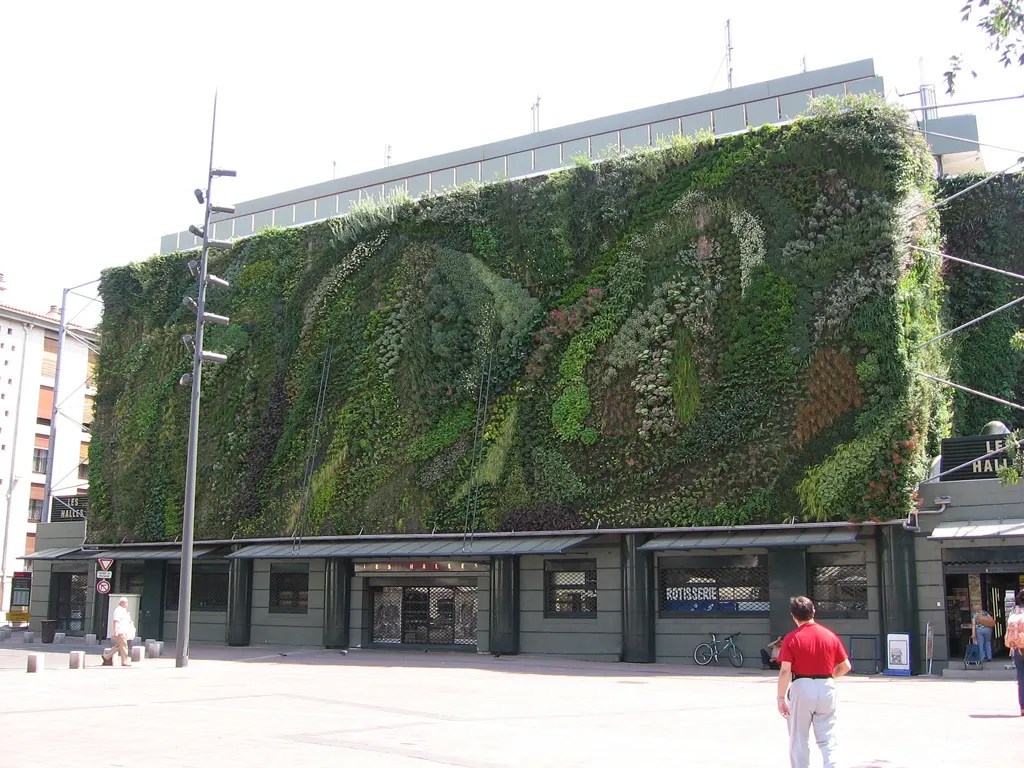 A fachada de Les Halles d'Avignon coberta pelo muro vegetal de plantas verdes, na Place Pie, com uma pessoa passando.