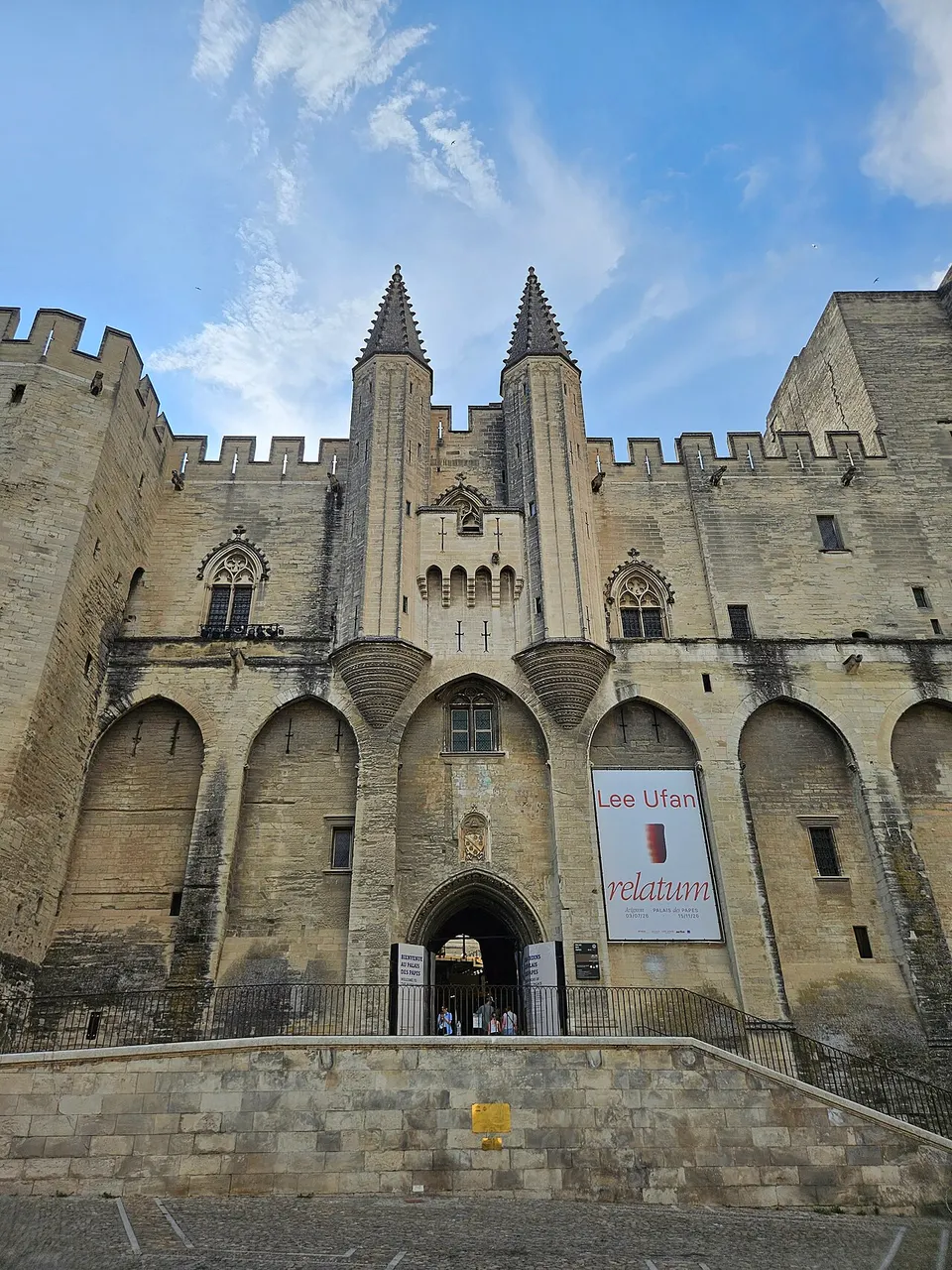 A fachada gótica do Palácio dos Papas vista de baixo, com as duas torrinhas pontudas, as ameias e a entrada no centro.