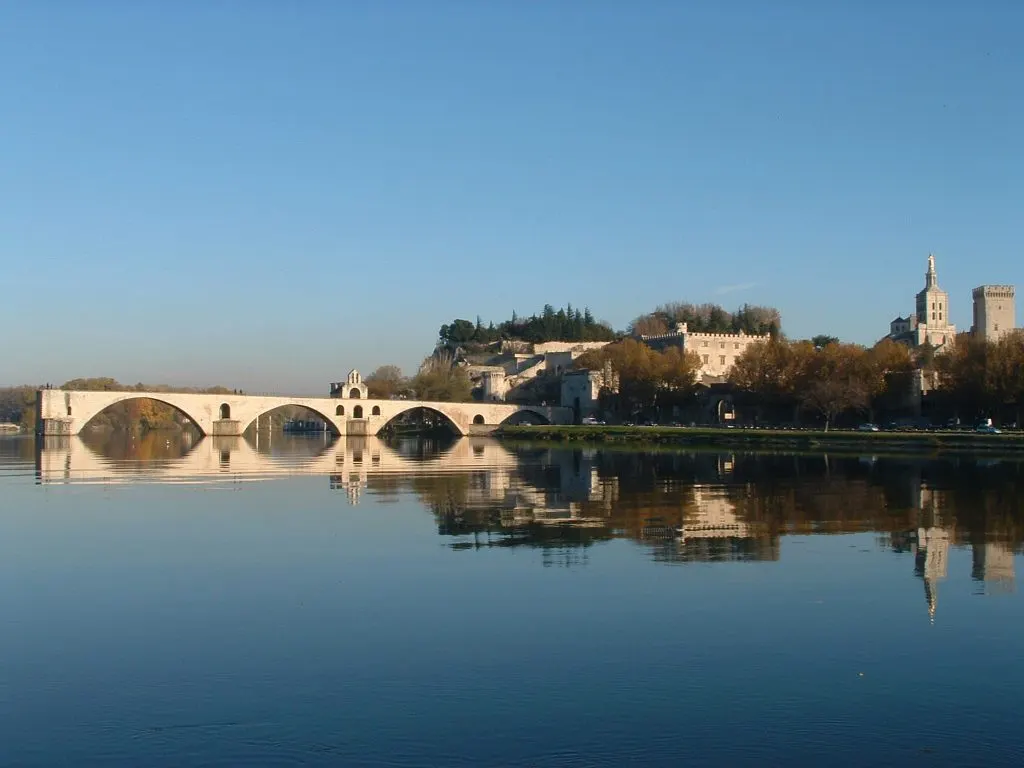 Os arcos que restam da Ponte Saint-Bénézet refletidos no Ródano calmo, com o Rochedo dos Doms e o Palácio dos Papas atrás.