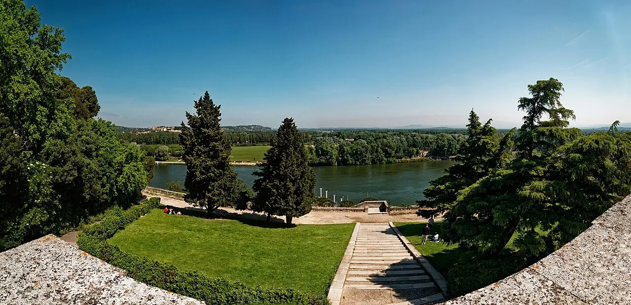 O jardim do Rocher des Doms com gramado, ciprestes e uma escadaria, e o Ródano e o vale ao fundo.