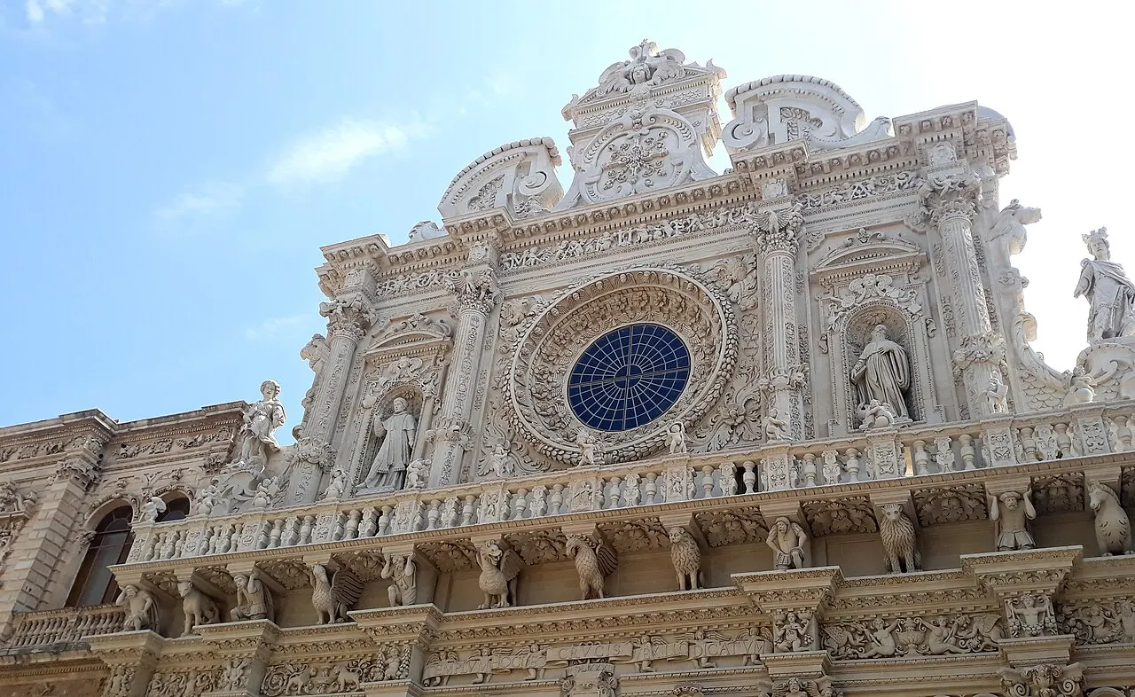 A fachada barroca de Santa Croce em pedra clara de Lecce, com a rosácea, estátuas e a balaustrada esculpida, vista de baixo.