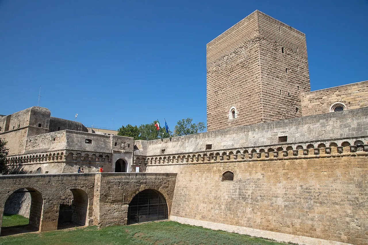 O Castelo de Bari com a torre quadrada, a muralha de pedra clara e a ponte de arcos sobre o fosso gramado.