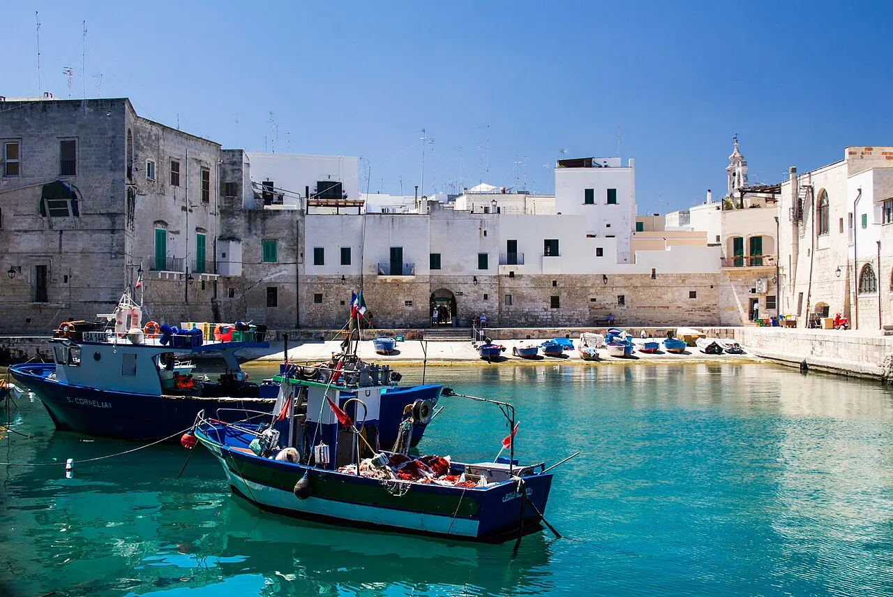 Barcos de pesca azuis na água turquesa do Porto Antico de Monopoli, com as casas brancas da cidade velha atrás.