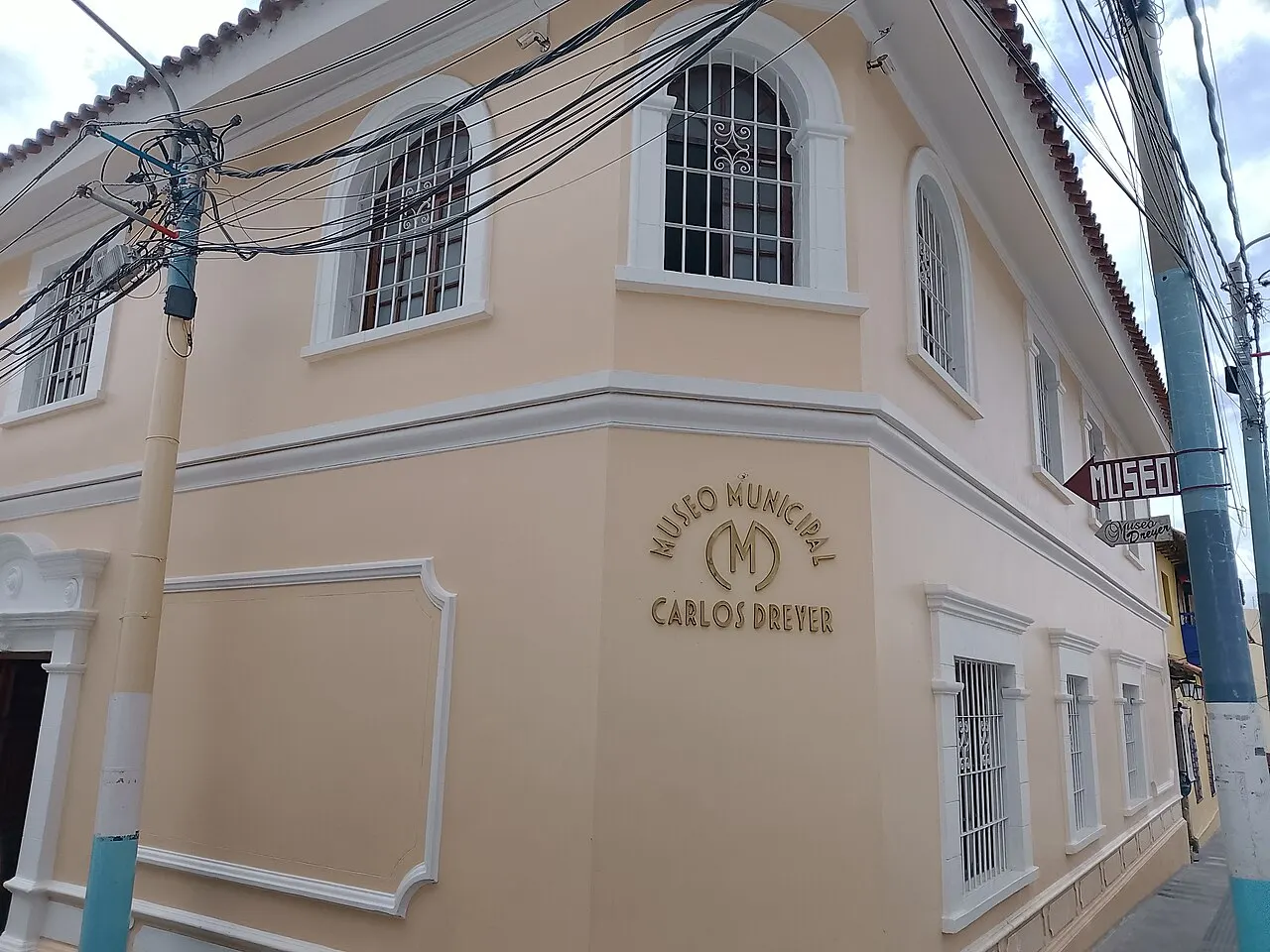 A esquina de um casarão creme de dois andares, com janelas em arco gradeadas e o nome do museu em letras douradas na parede.