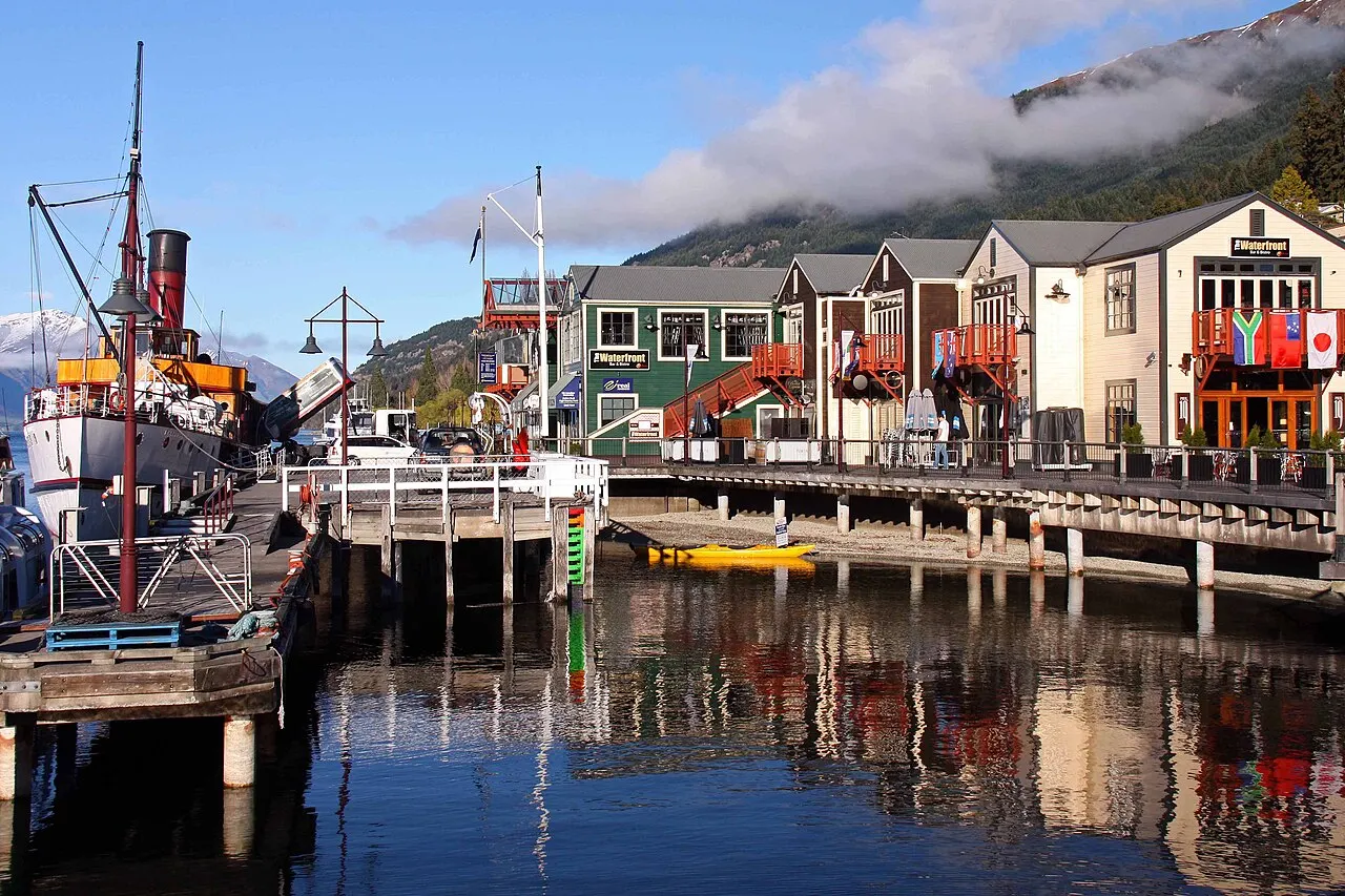 Cais de madeira do Steamer Wharf, com casas coloridas, um barco a vapor e montanhas ao fundo.