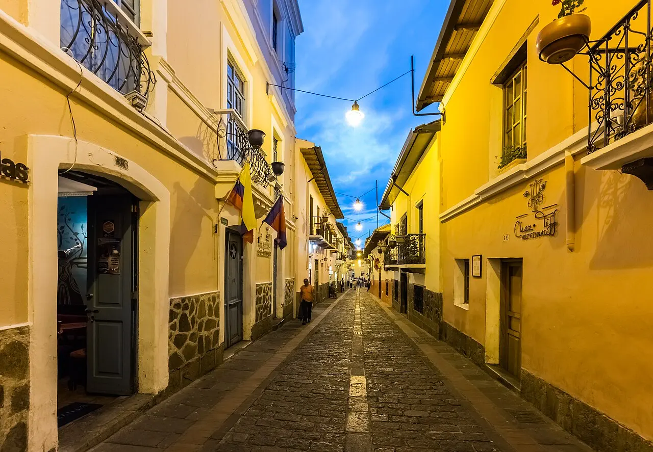 Rua estreita e de pedra, a Calle La Ronda, com casas amarelas e lampiões acesos no fim do dia.