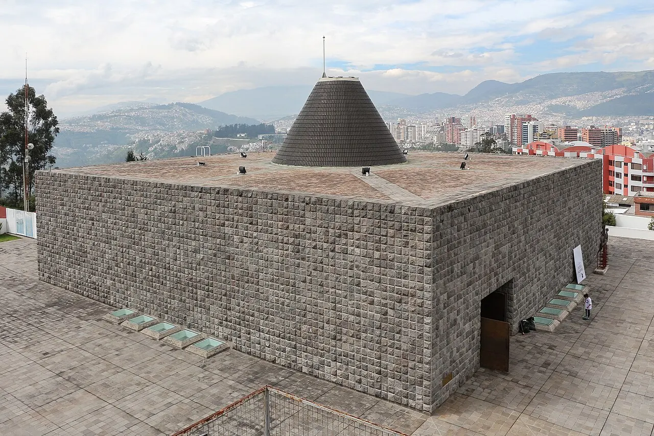 Capilla del Hombre, em Quito: um bloco baixo de paredes de pedra aparente, coberto por um telhado cônico, com a cidade e o vale ao fundo.