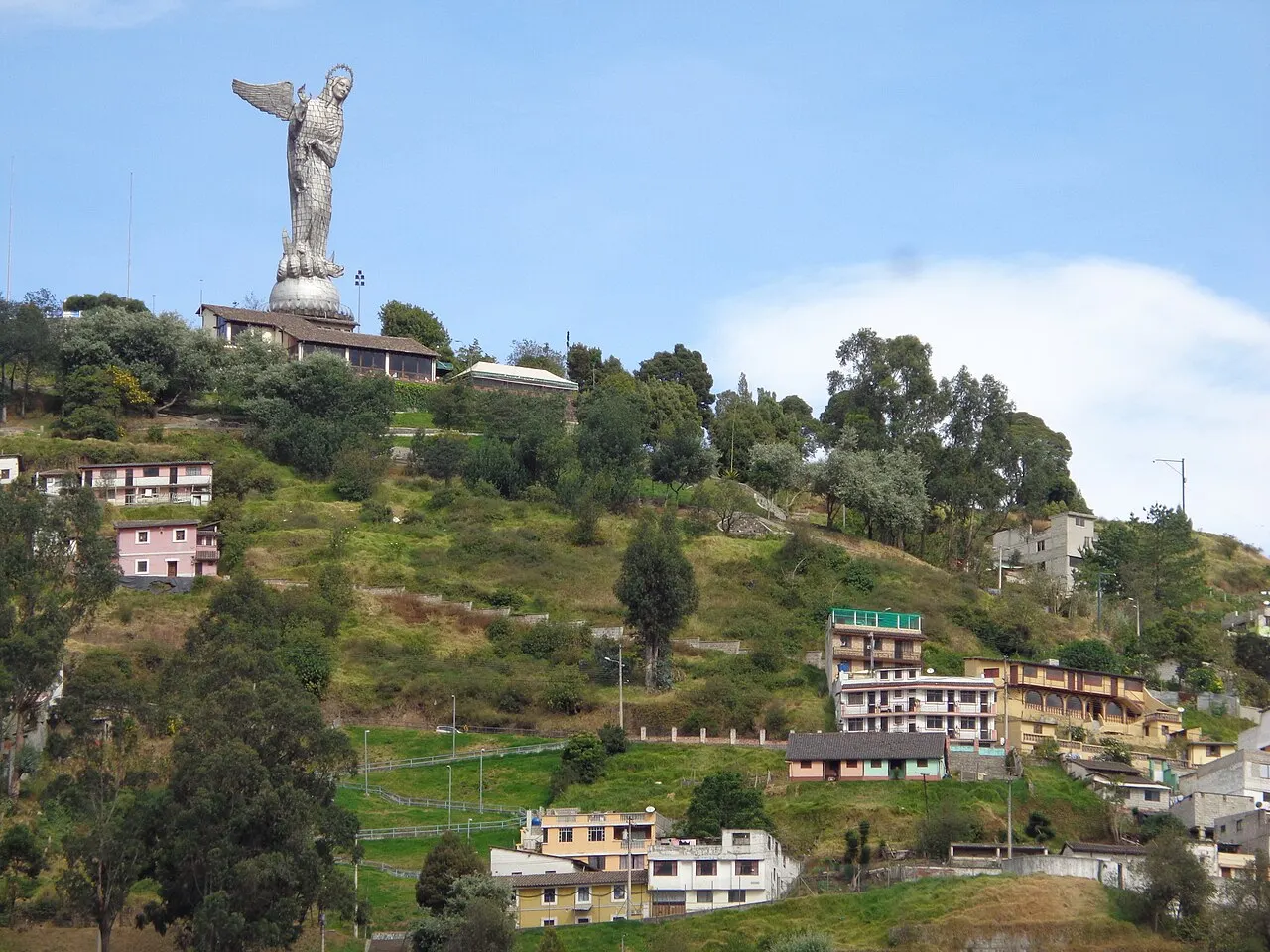 A colina do Panecillo, com a estátua da Virgem no topo e casas e vegetação na encosta, sob céu azul.