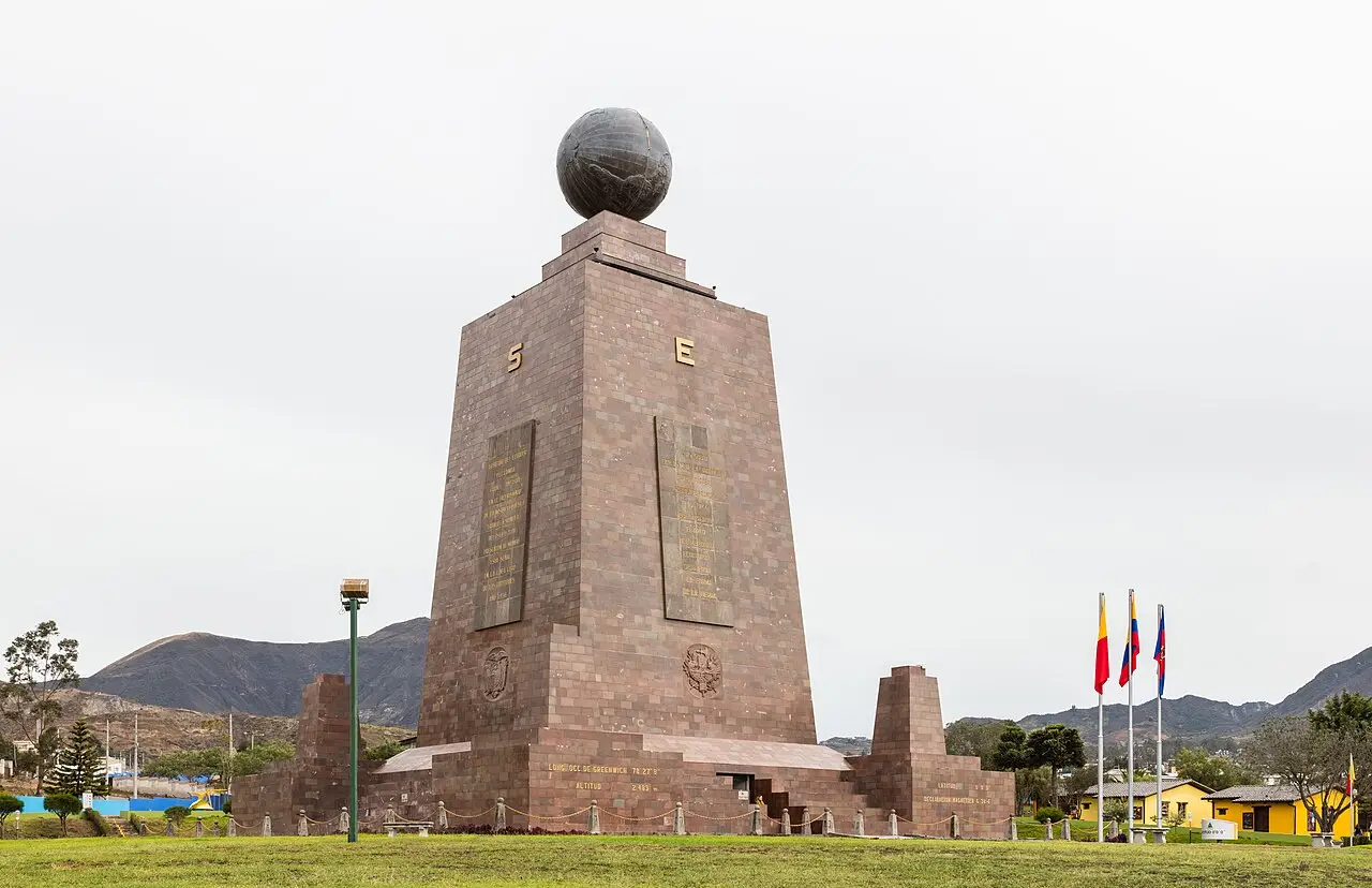 Monumento da Mitad del Mundo, pirâmide de pedra com o globo no topo e bandeiras ao lado.