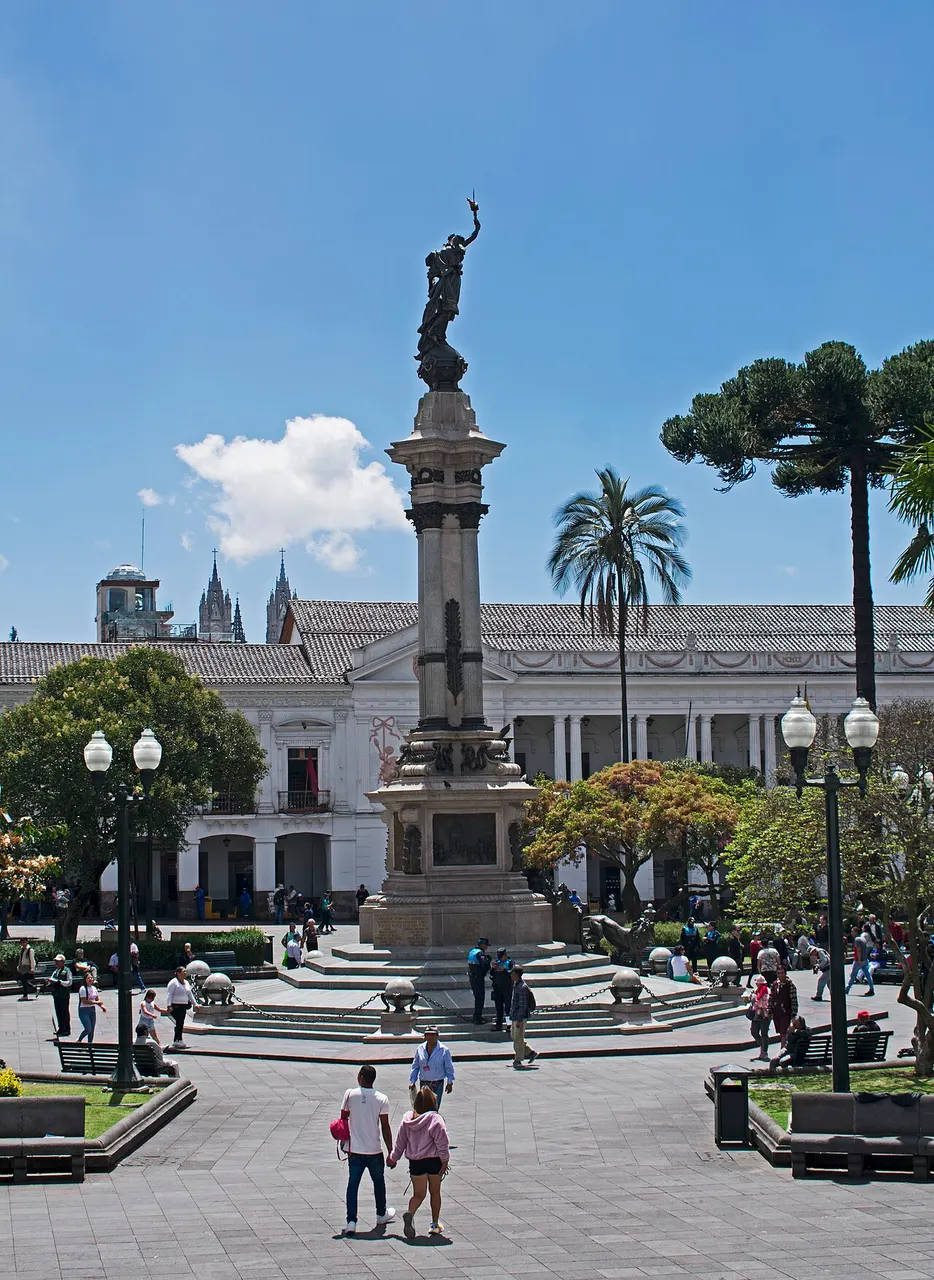 Monumento à Independência, uma coluna com estátua no alto, no centro da Plaza Grande de Quito, visto da escadaria da catedral.