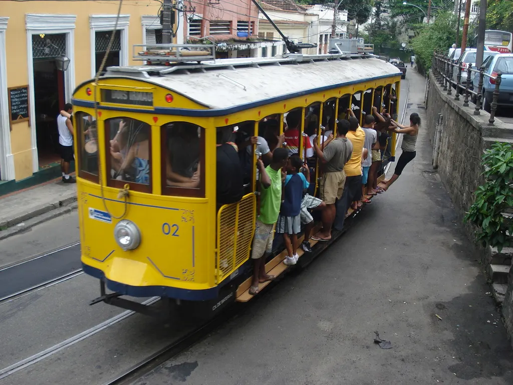 Bonde amarelo de Santa Teresa lotado, com passageiros nos estribos, numa rua perto do Largo do Guimarães.