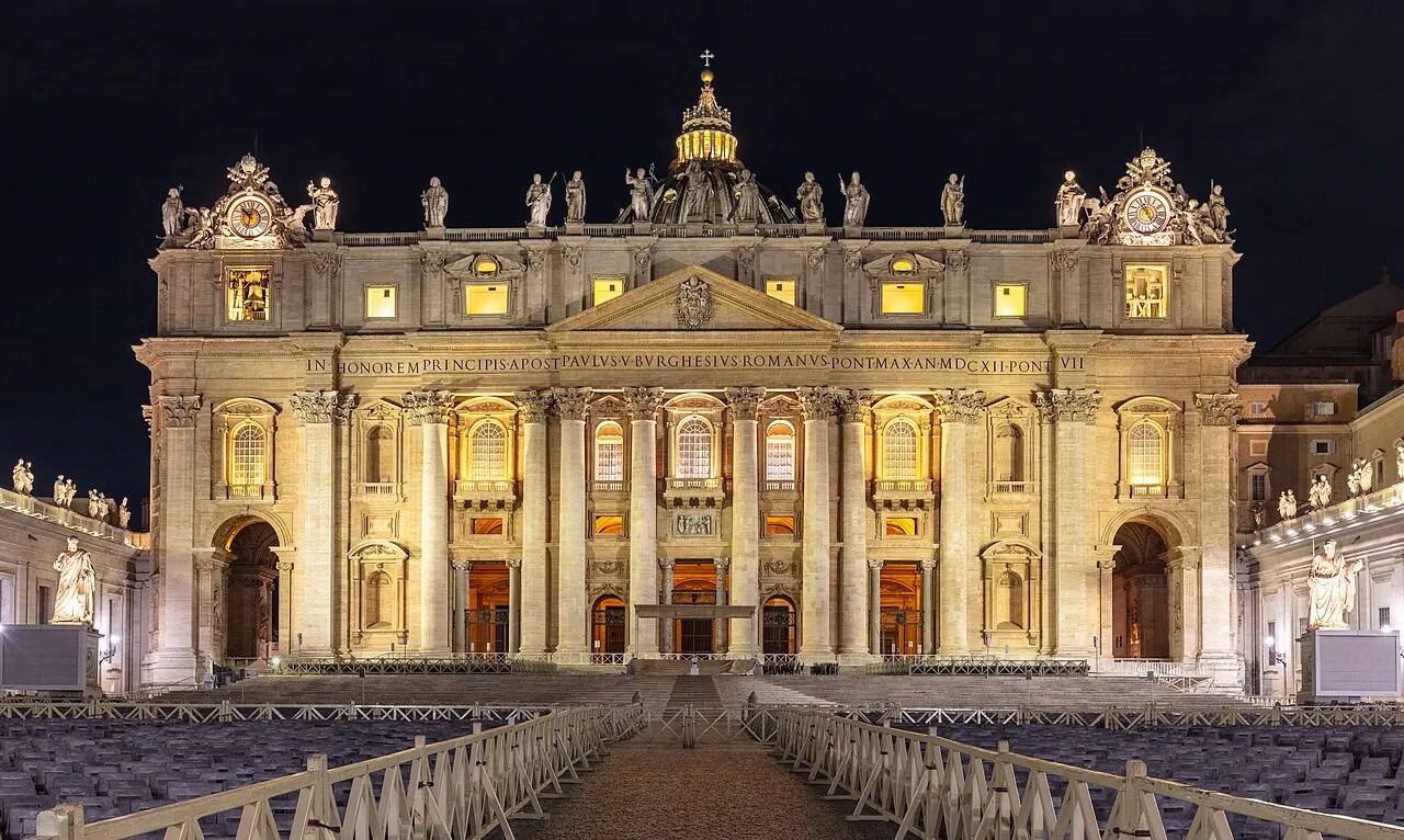 La façade de la basilique Saint-Pierre éclairée la nuit, avec la lanterne de la coupole visible derrière.