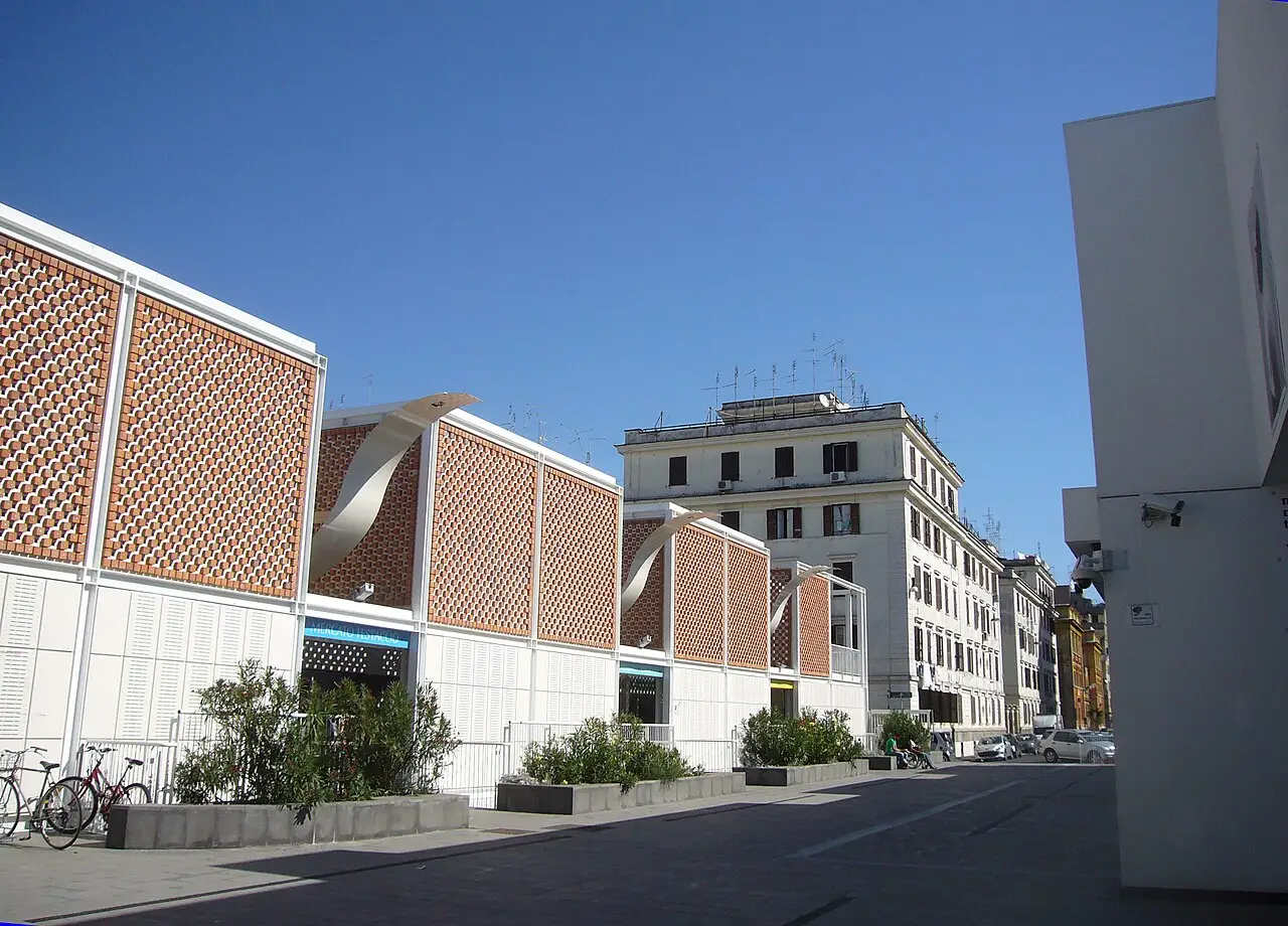 Bâtiment clair en brique avec une toiture en dents de scie et l'enseigne du marché.