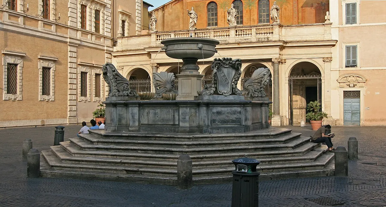 Fonte octogonal de degraus na Piazza di Santa Maria in Trastevere, em Roma, diante de fachadas ocre.