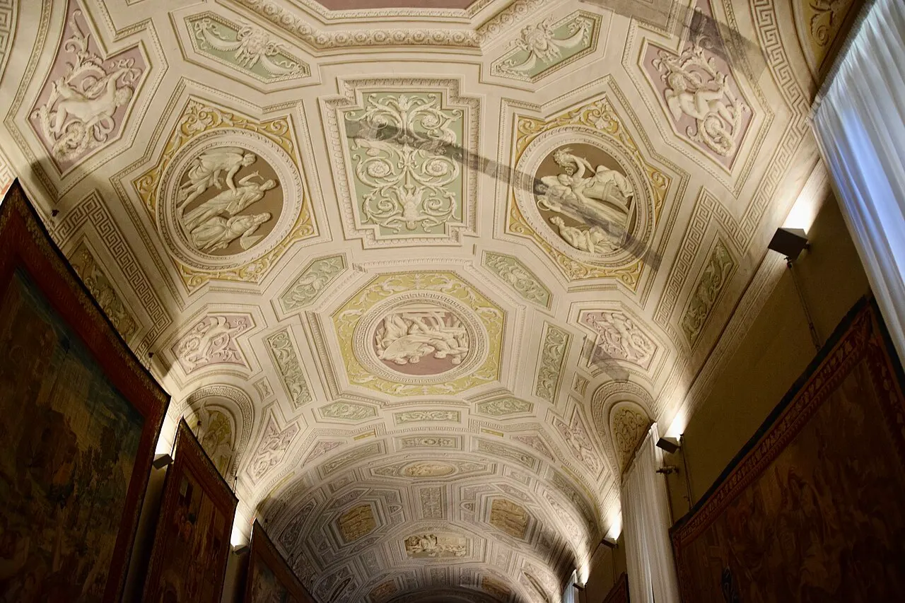 Galeria dos Museus Vaticanos, com teto abobadado decorado com estuques e medalhões pintados e tapeçarias nas paredes.