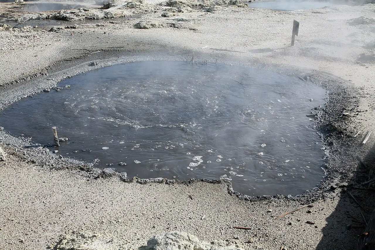 A pool of grey water bubbling and steaming on pale mineral ground.