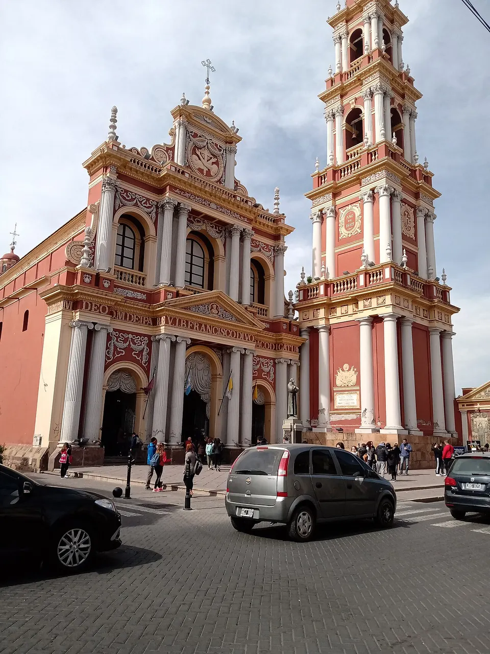 A igreja de San Francisco, em Salta, pintada de vermelho e creme, com a torre alta do campanário à direita e carros na rua.