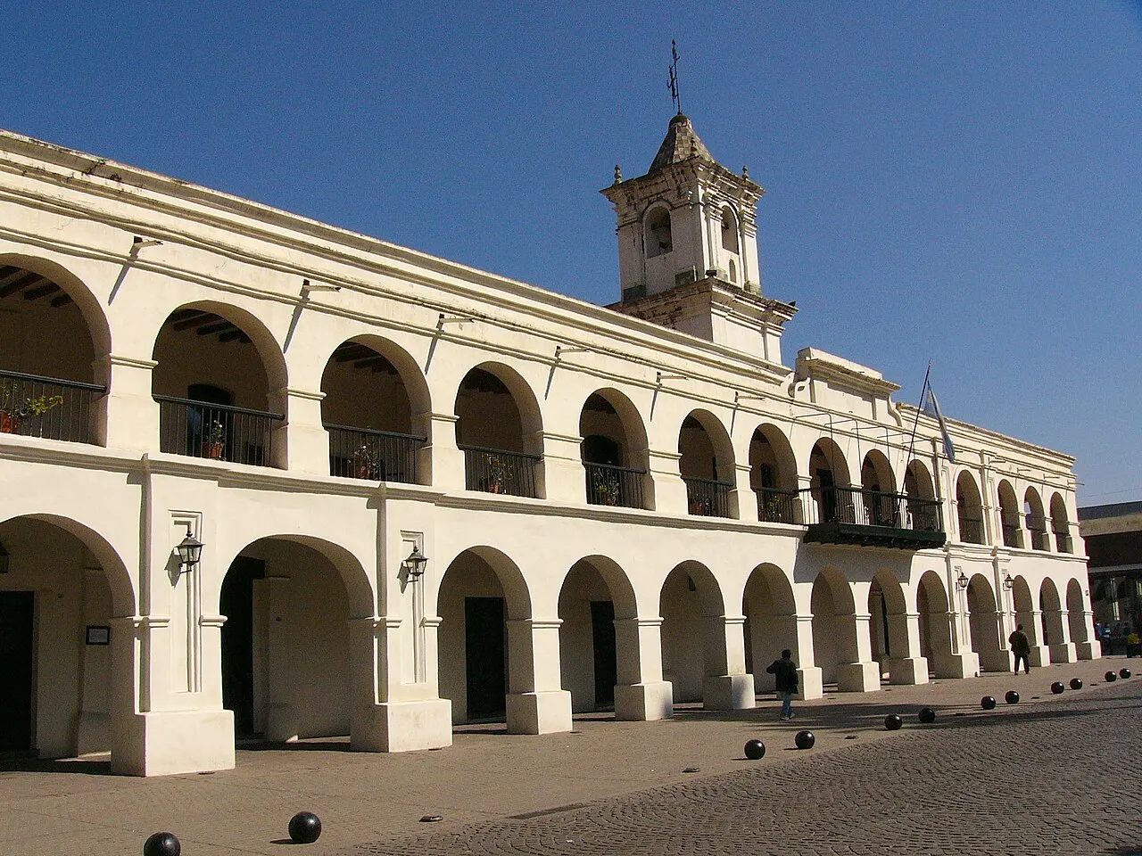 El Cabildo de Salta, un edificio colonial blanco con dos hileras de arcos y una torre pequeña en el centro, bajo el cielo azul.