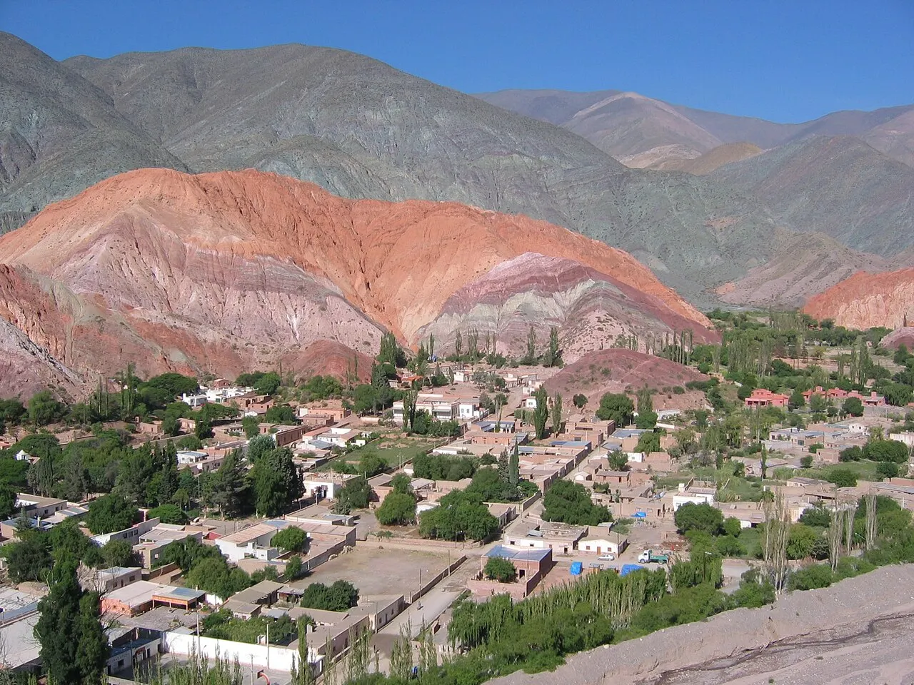 El Cerro de los Siete Colores, con franjas de roca rosa, roja y verde, detrás de las casas bajas y los árboles de Purmamarca.