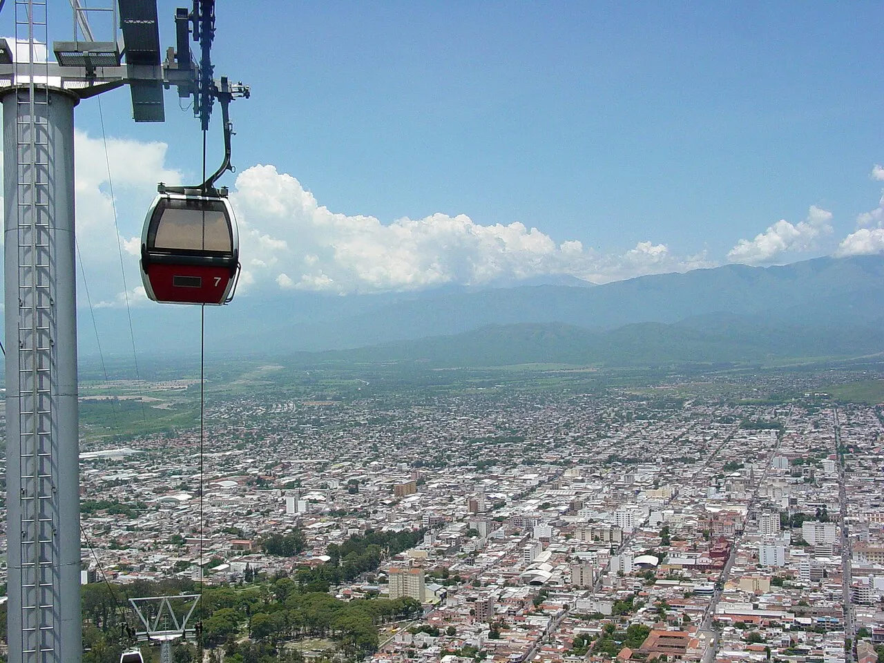 Uma cabine vermelha do teleférico do Cerro San Bernardo pendurada sobre a cidade de Salta, que se estende até as montanhas.