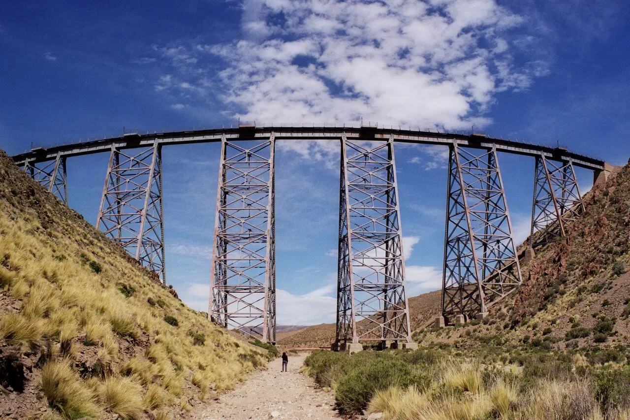 El Viaducto La Polvorilla, un puente ferroviario de acero en curva sobre torres reticuladas, que cruza un valle seco bajo el cielo azul.