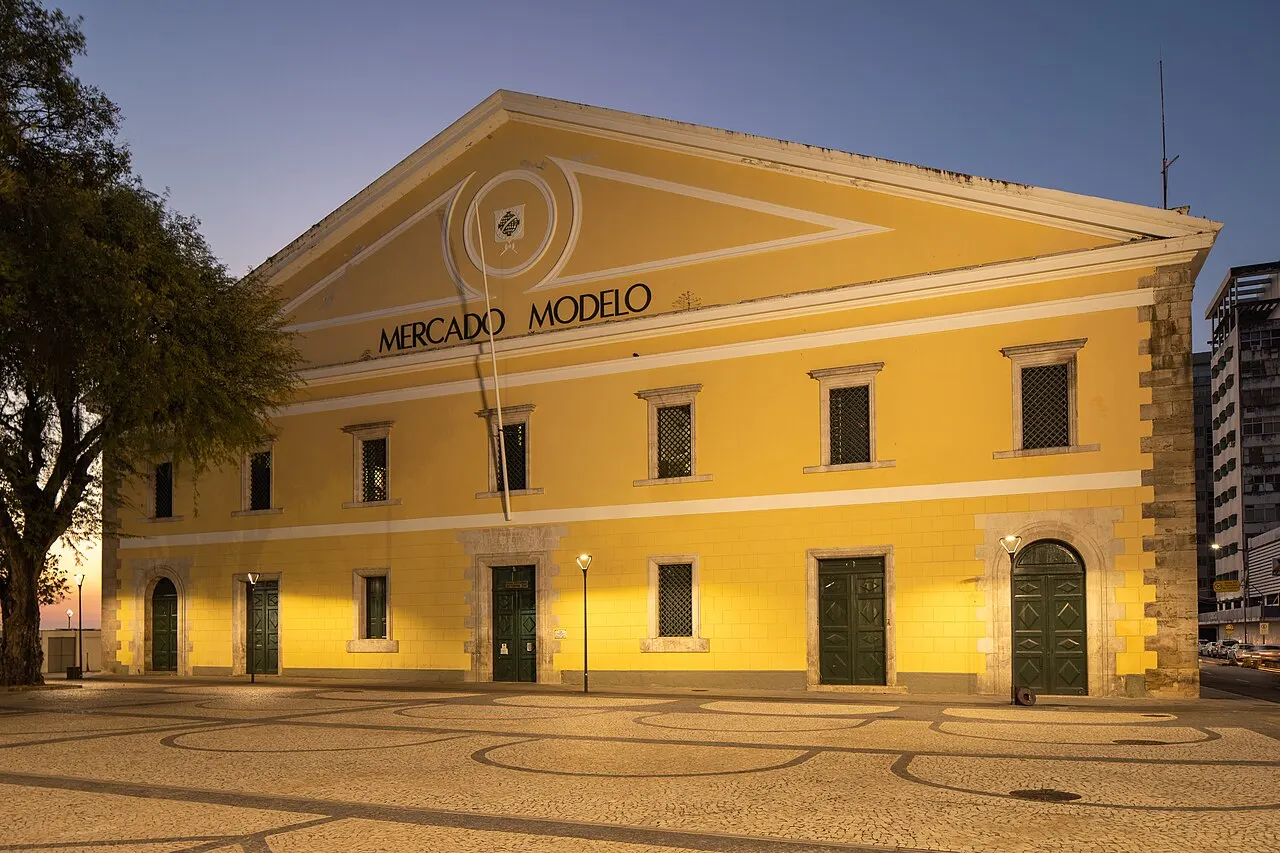 Prédio amarelo do Mercado Modelo, em Salvador, com o letreiro na fachada e palmeiras ao lado.