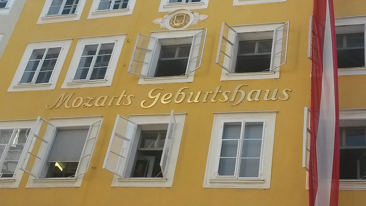 A fachada amarela da casa natal de Mozart, com o letreiro «Mozarts Geburtshaus» entre as janelas e uma bandeira vermelha e branca.