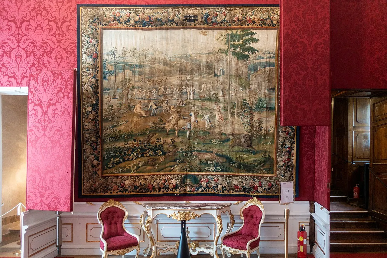 Uma sala dos aposentos do príncipe-arcebispo no DomQuartier, com paredes de tecido vermelho, uma tapeçaria grande e cadeiras estofadas.