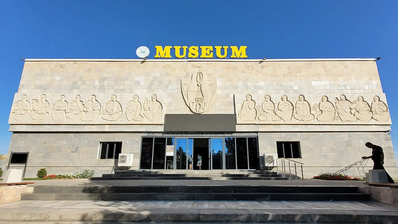 Fachada do Museu de Afrasiab, prédio baixo de pedra clara com friso de figuras e a palavra MUSEUM no topo.